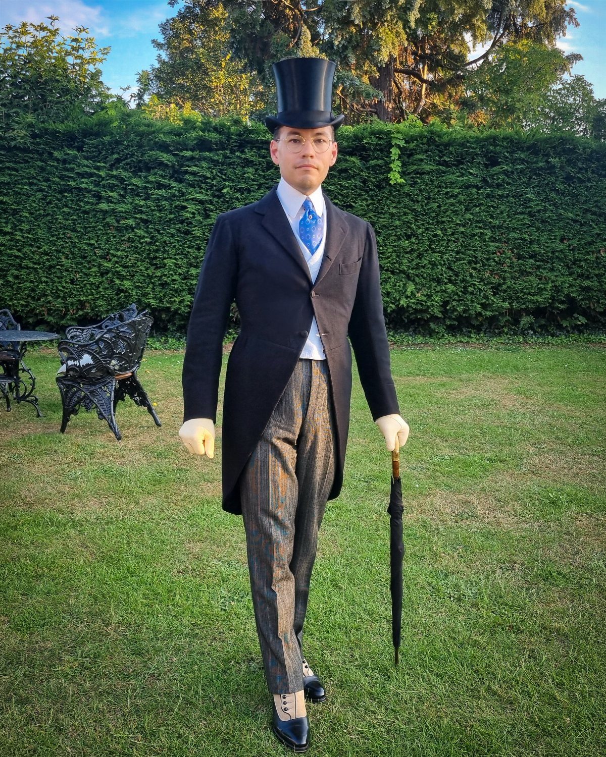Man in 1880s style fashion wearing a top hat and morning coat on grass