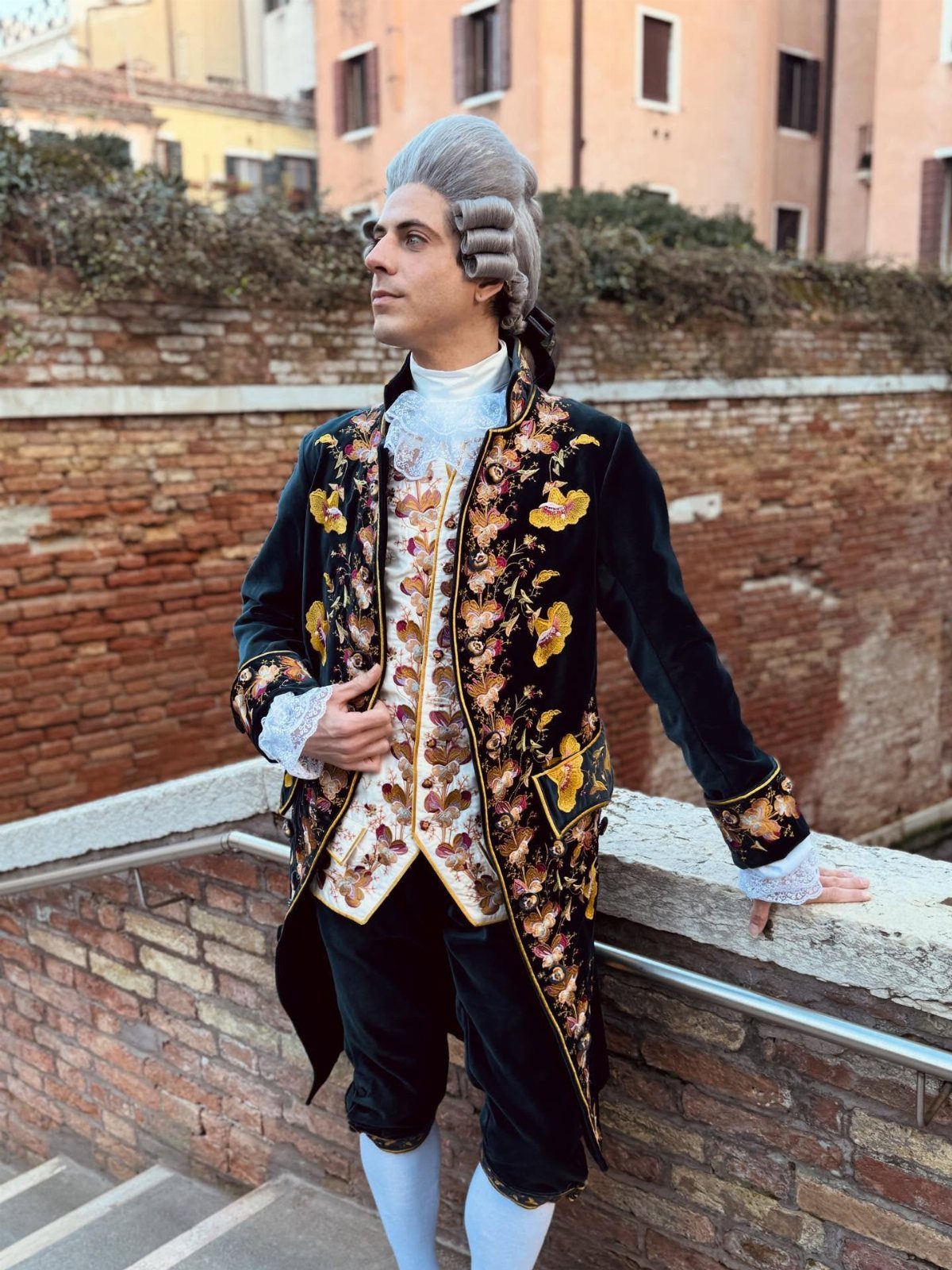 Man in ornate 18th century men's fashion with powdered wig and embroidered velvet coat.