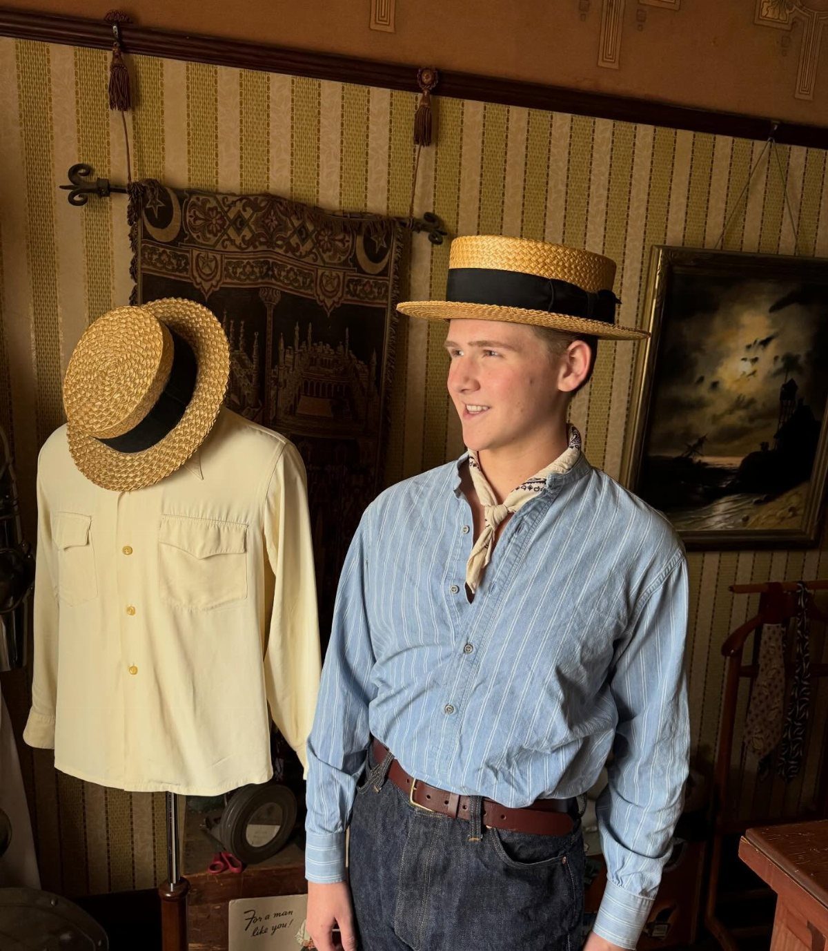 Young man in a straw boater hat and blue striped shirt in vintage room