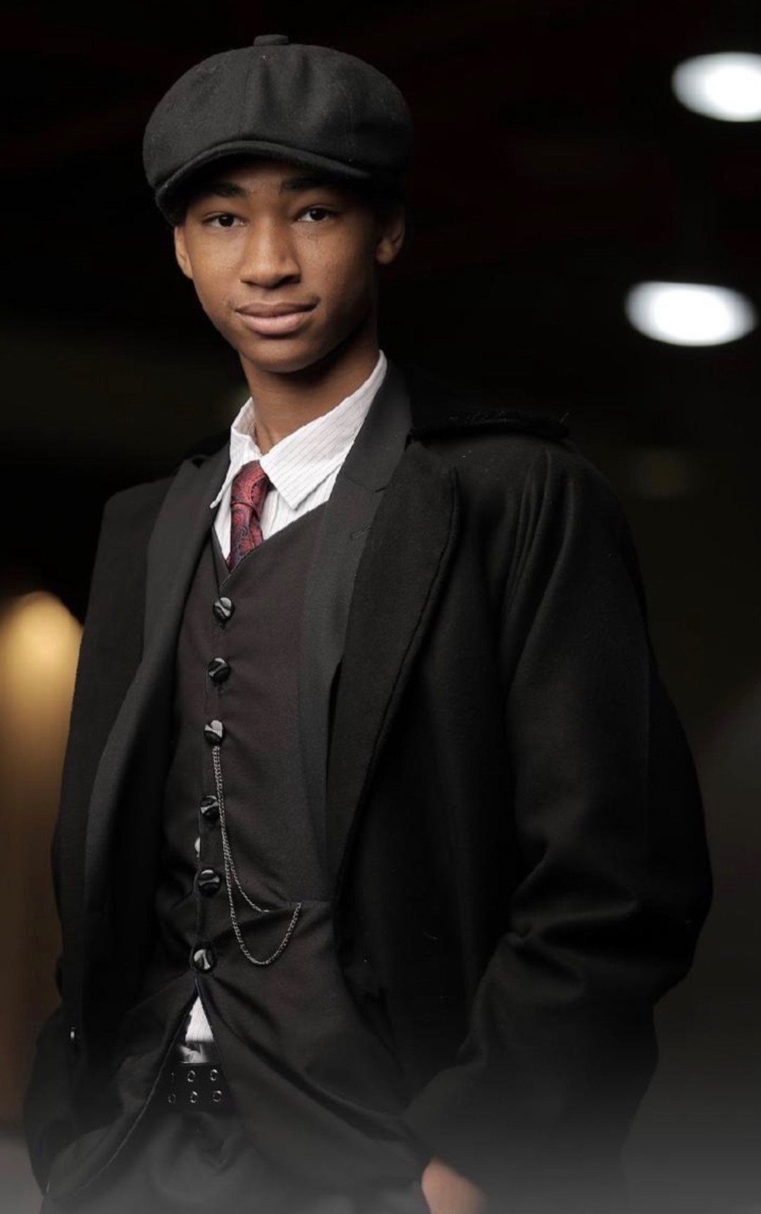 Young Black man wearing 1920s working-class attire including a newsboy cap and waistcoat.
