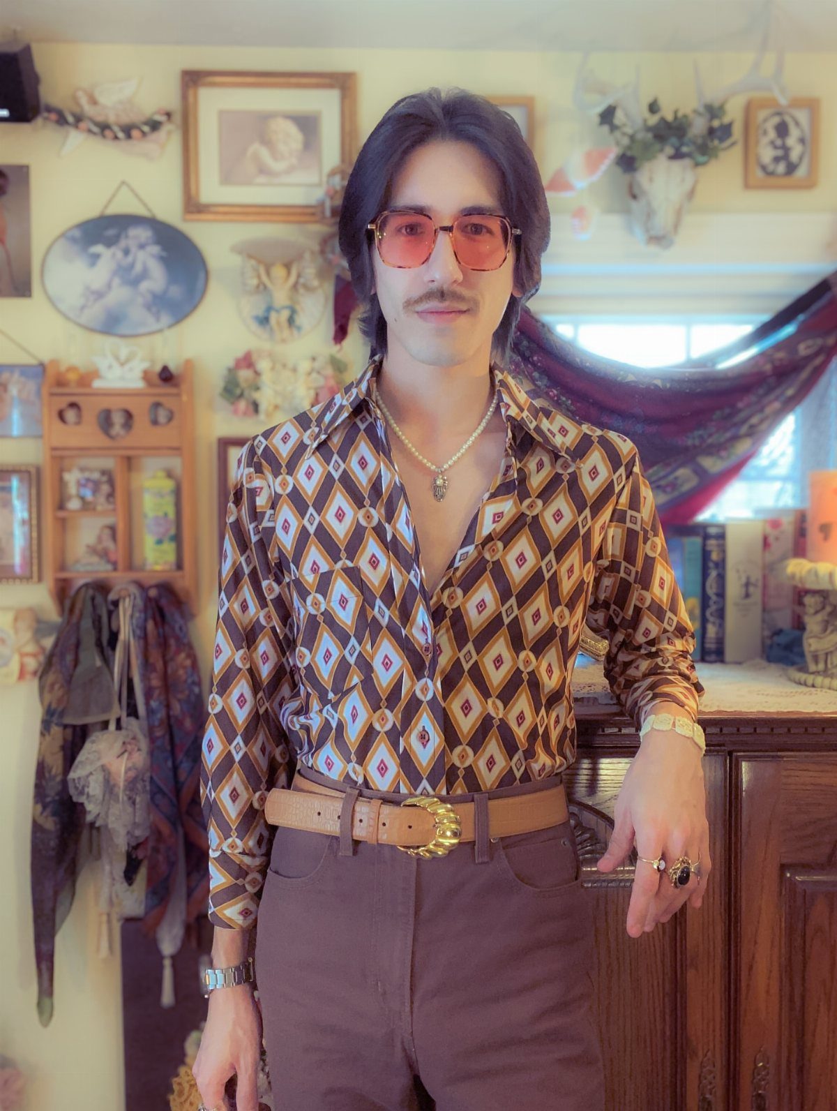 Man wearing a bold diamond-patterned brown shirt and brown trousers in a vintage room.