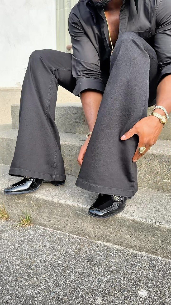 Man in black flared trousers and patent leather loafers sitting on concrete steps.