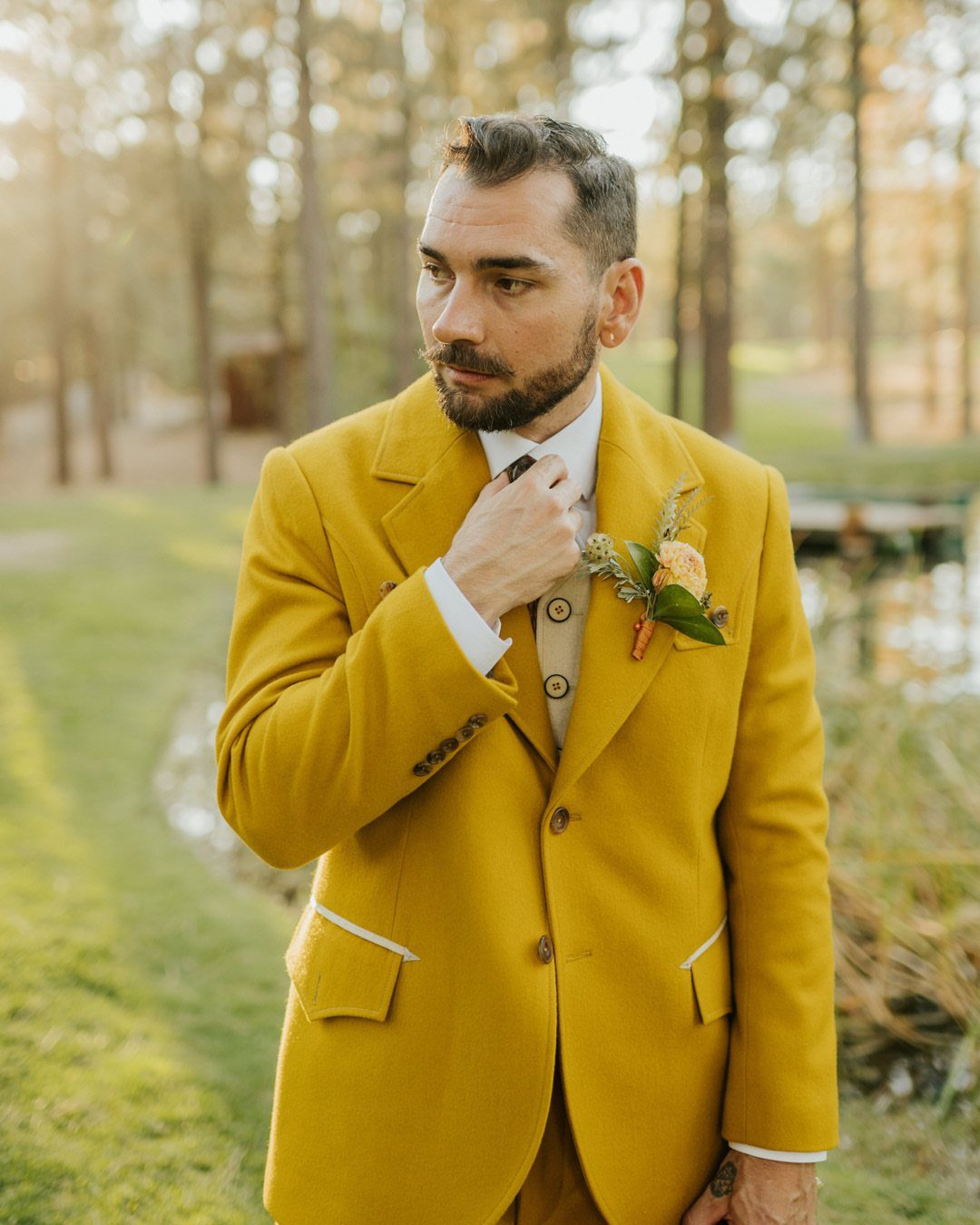 Man in a mustard yellow suit and vest standing in a sunny wooded area.