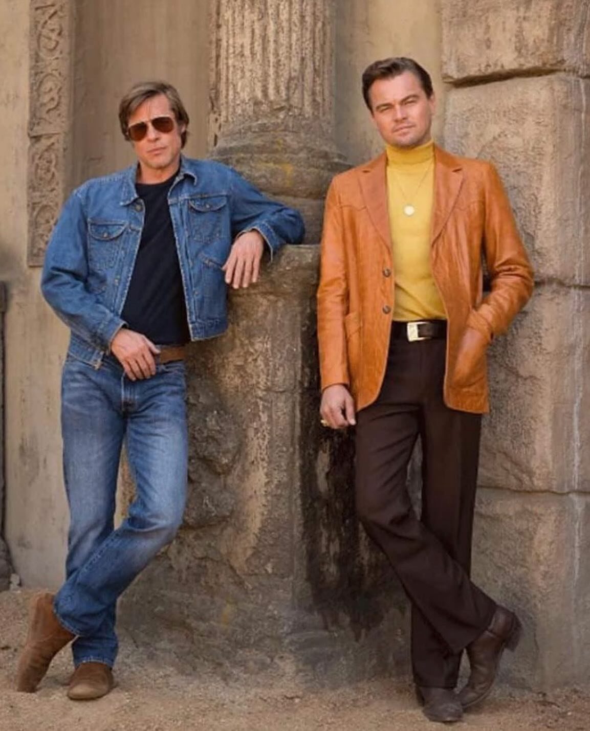 Two men in 1970s style clothing, one wearing a yellow turtleneck and leather blazer.