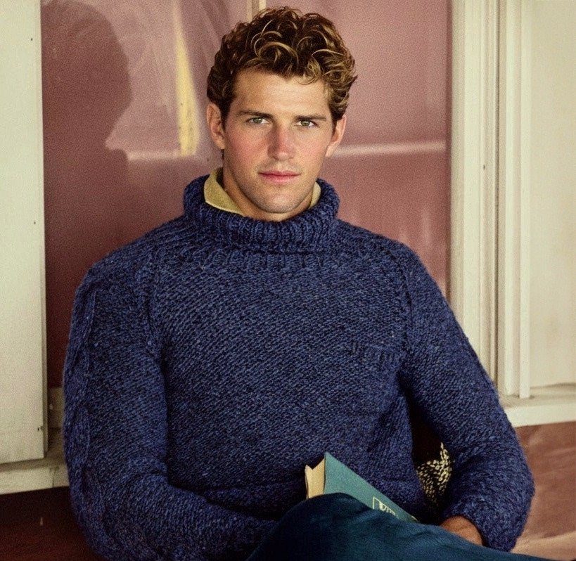 Man with curly hair wearing a blue knit turtleneck sweater and yellow collar.