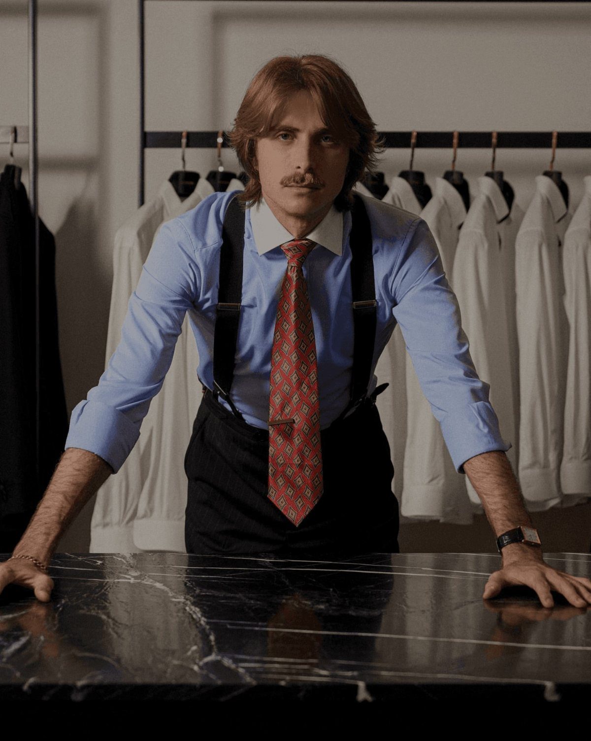 Man with mustache wearing blue shirt, red tie, and suspenders in a clothing store.