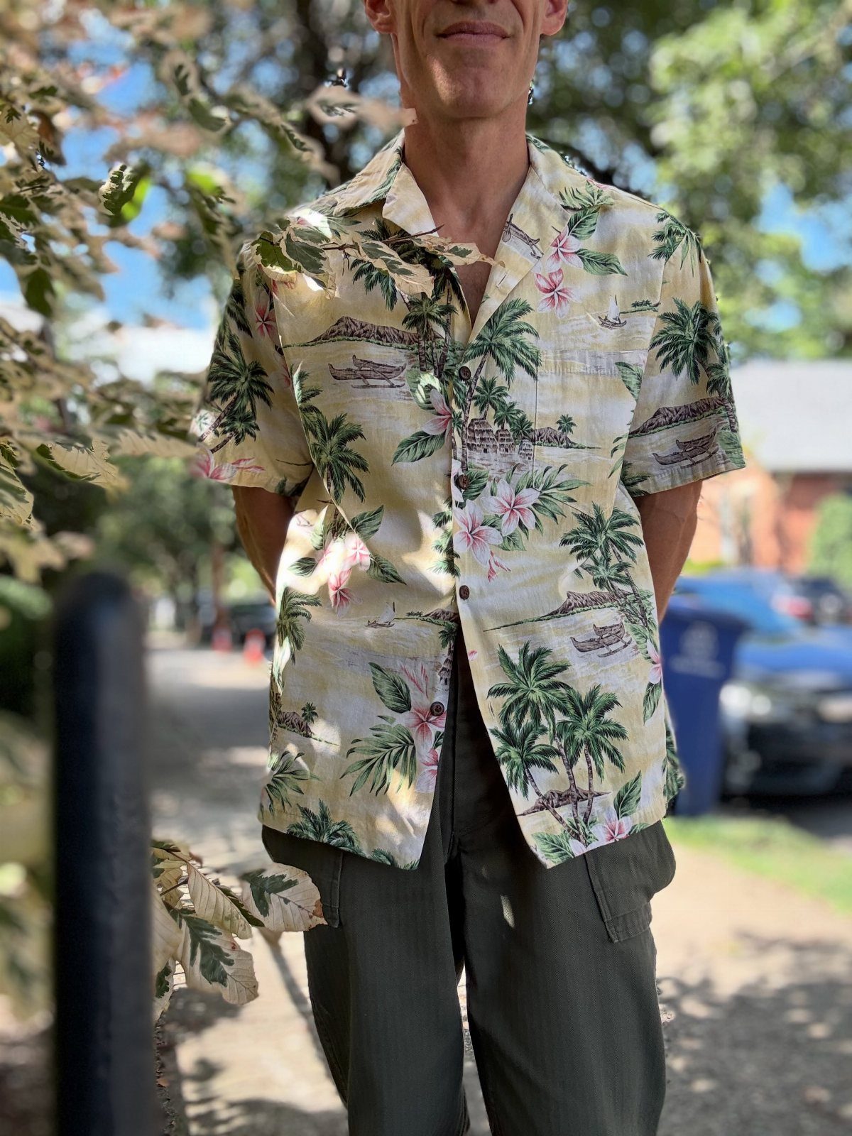 Man wearing a yellow Hawaiian shirt with palm tree prints and olive trousers.