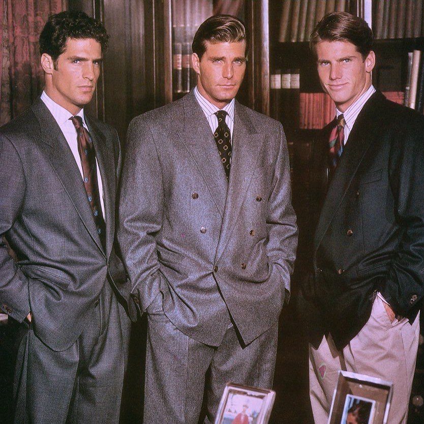 Three men wearing oversized 1980s business suits and ties in a library setting.