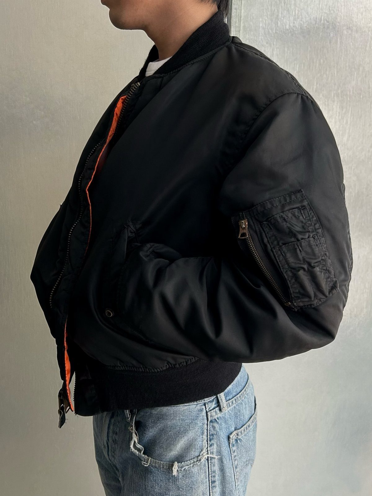 Black bomber jacket with orange lining and sleeve pocket worn with blue jeans.