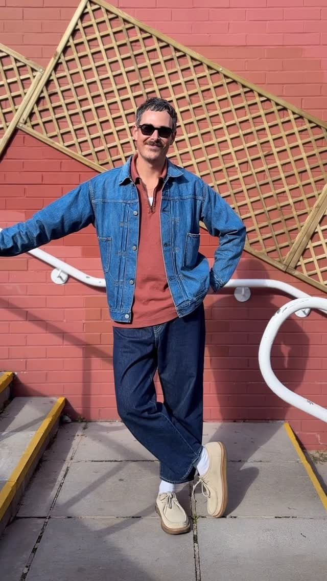 Man wearing a blue denim jacket and matching jeans with a rust polo shirt.
