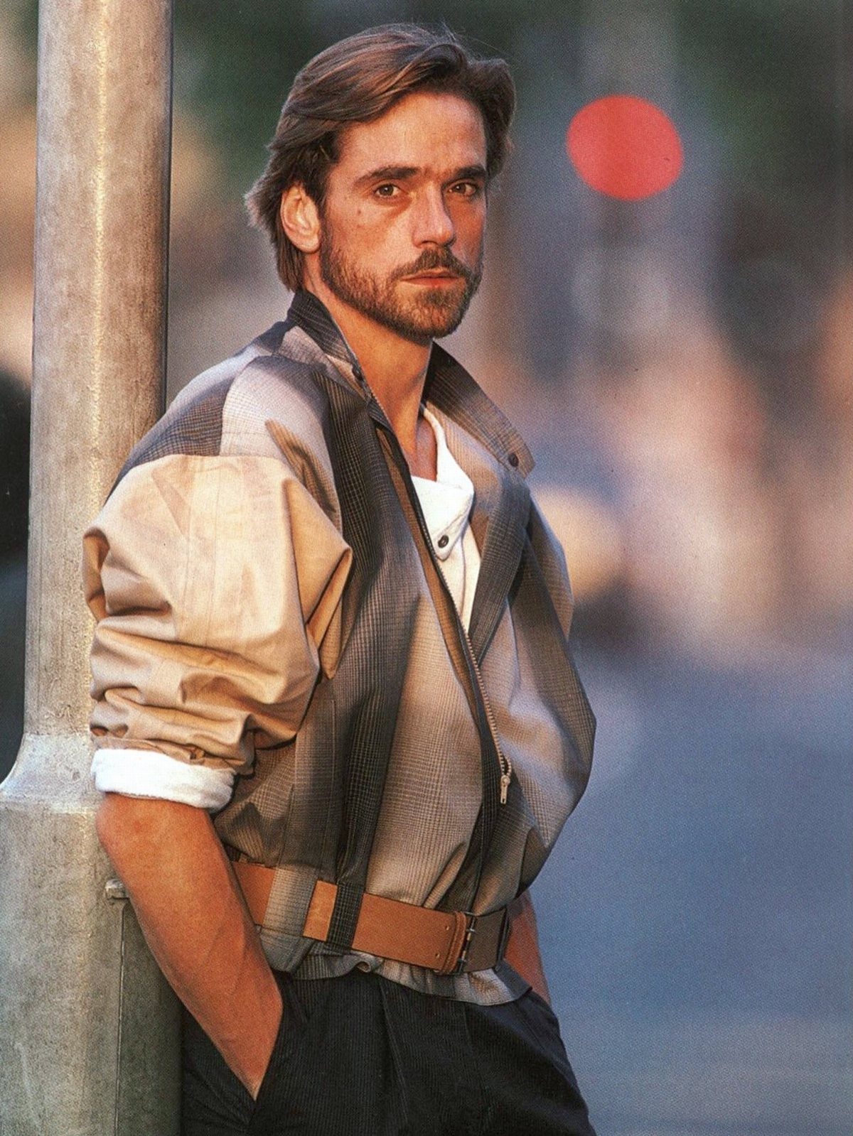 Man in 1980s fashion wearing an oversized patterned jacket and wide tan belt.