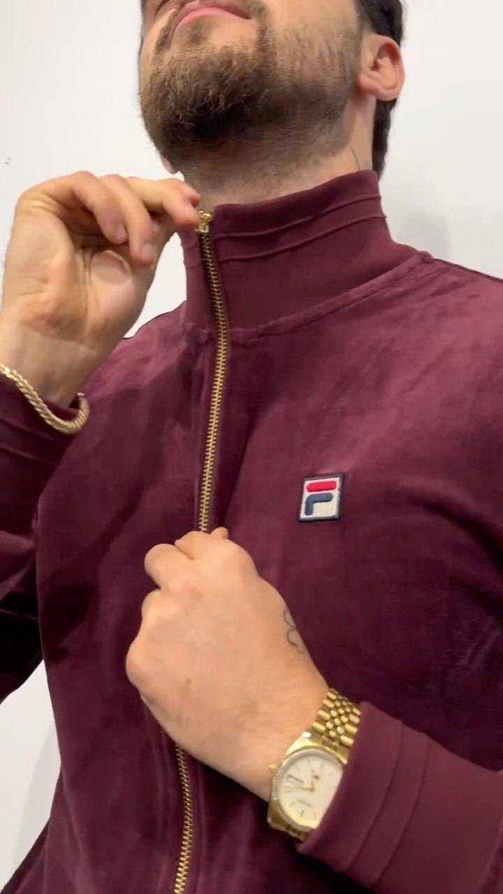 Man wearing a maroon velvet Fila track jacket with gold jewelry.