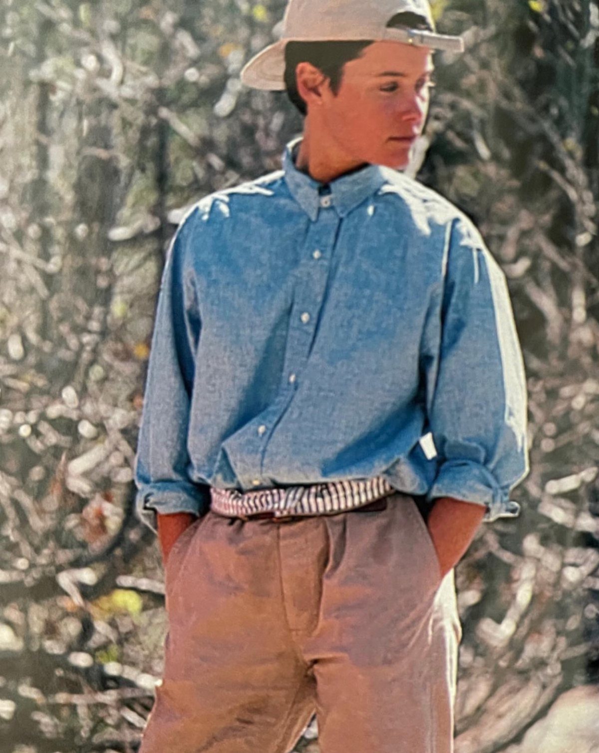 Young man in a blue button-down shirt, tan trousers, and beige baseball cap.