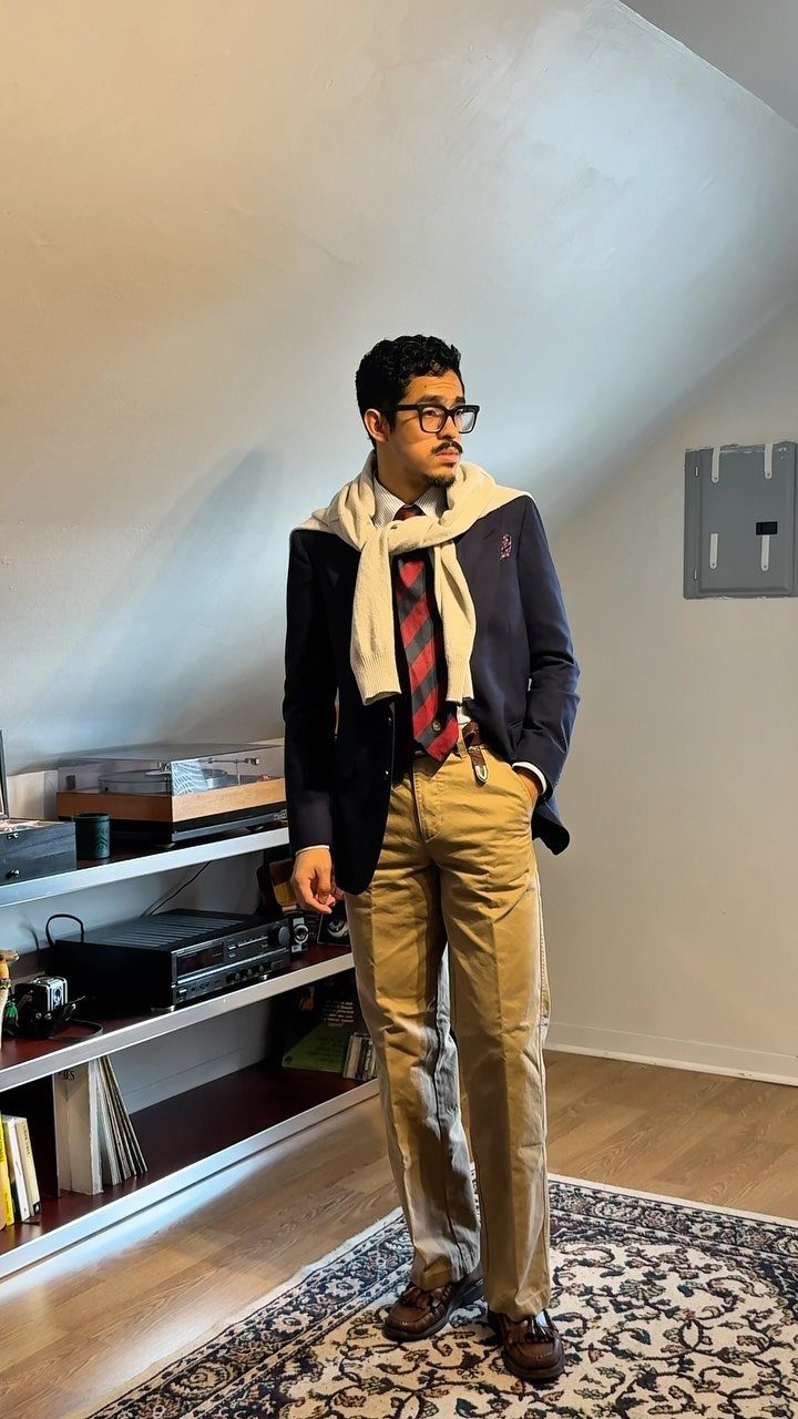 Man in navy blazer and khaki pants with sweater draped over shoulders.