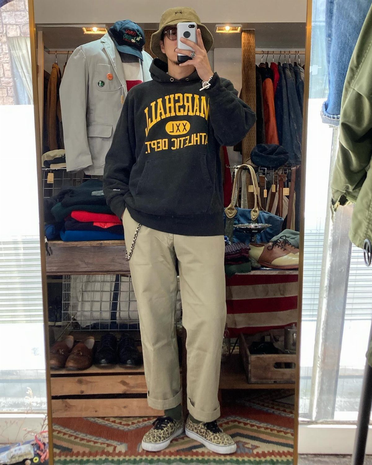 Person wearing a tan bucket hat, black hoodie, and beige trousers in a store.