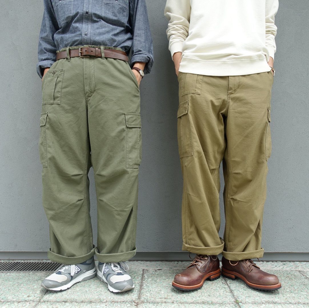 Two men wearing loose olive and tan cargo pants with cuffed hems.