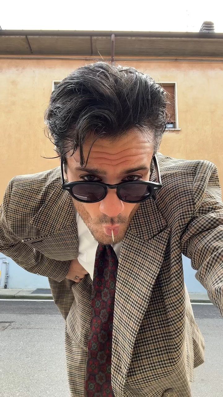 Man in a brown checkered blazer and sunglasses posing for a portrait outdoors.
