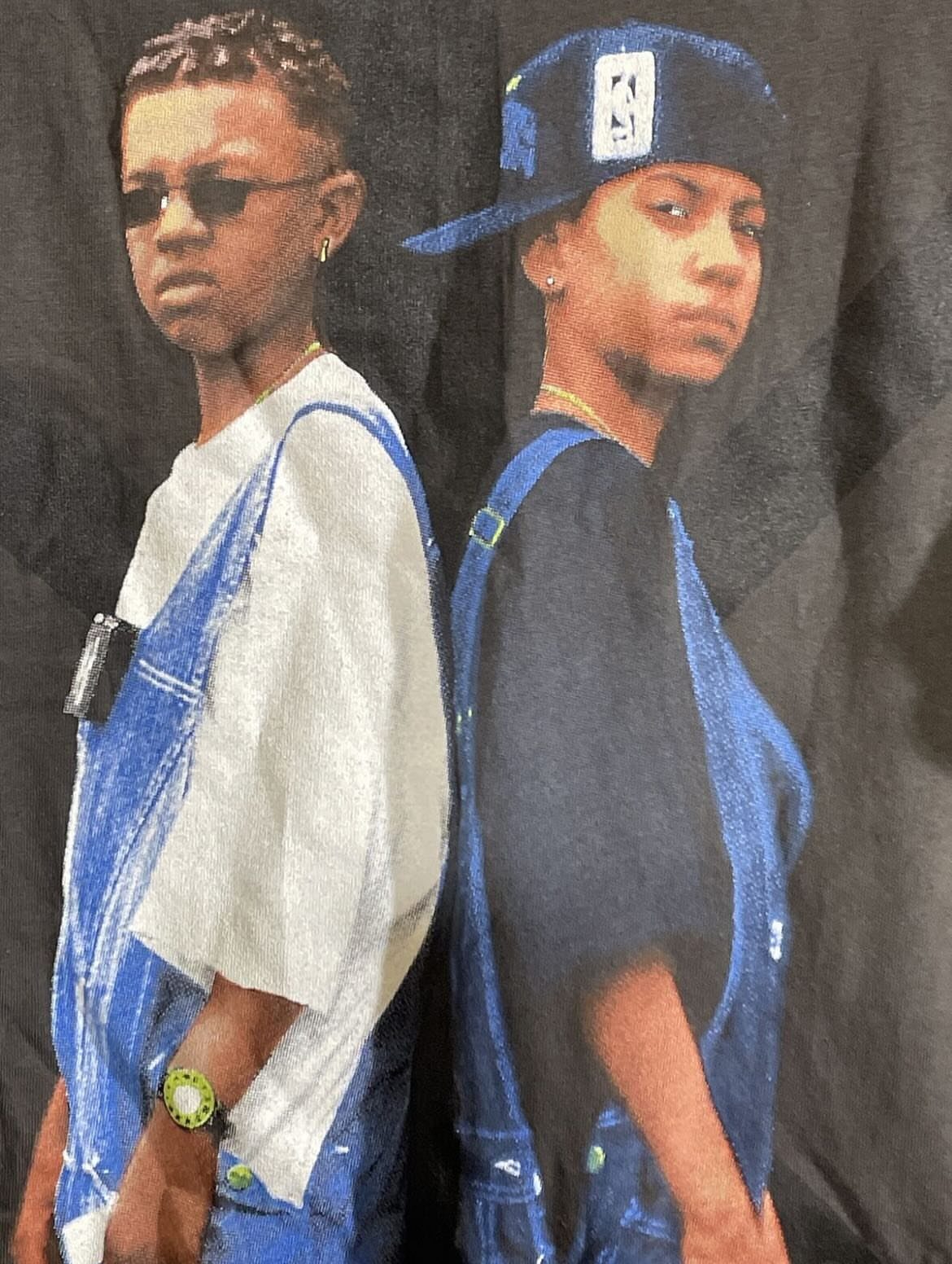 Two young men wearing blue denim overalls and t-shirts in a studio portrait.