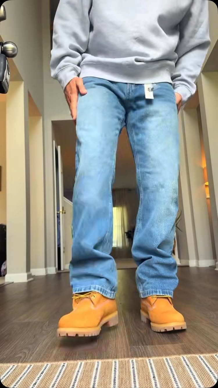 Person wearing a grey sweatshirt, baggy light blue jeans, and tan work boots.
