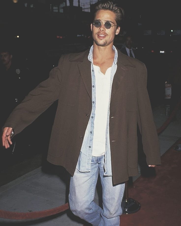 Man in oversized brown blazer, light blue shirt, and jeans on red carpet.