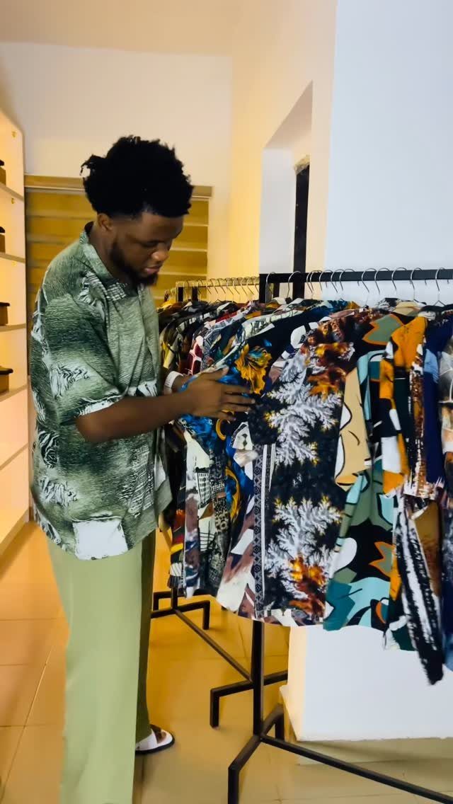 Man in a green patterned shirt browsing a rack of colorful patterned shirts.