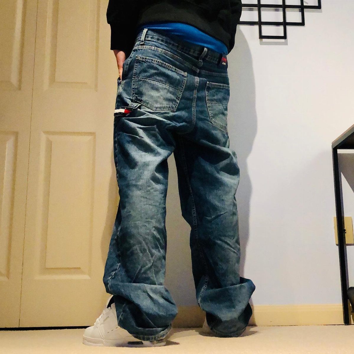 Person wearing oversized baggy blue denim jeans and white sneakers standing indoors.