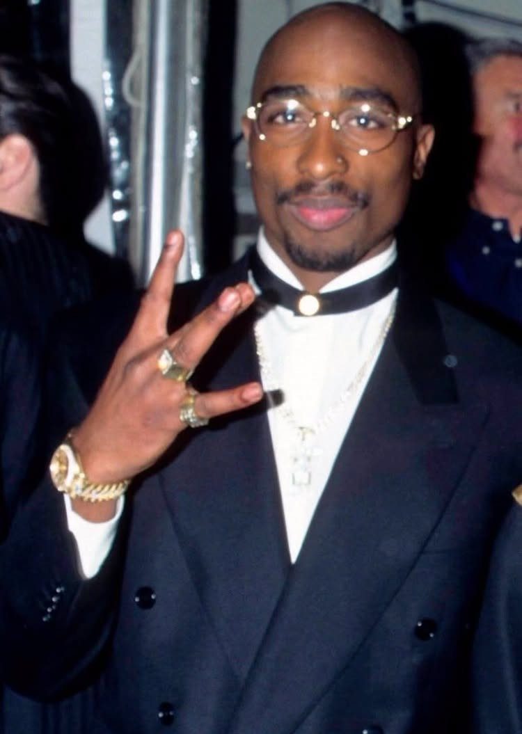 Man in a black double-breasted blazer and gold jewelry posing for a photo.