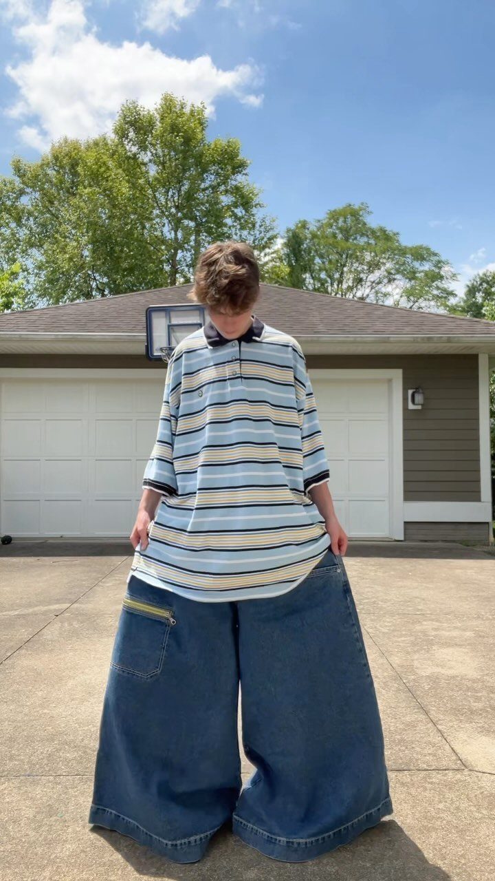 Person wearing an oversized striped polo and wide-leg jeans in a residential driveway.