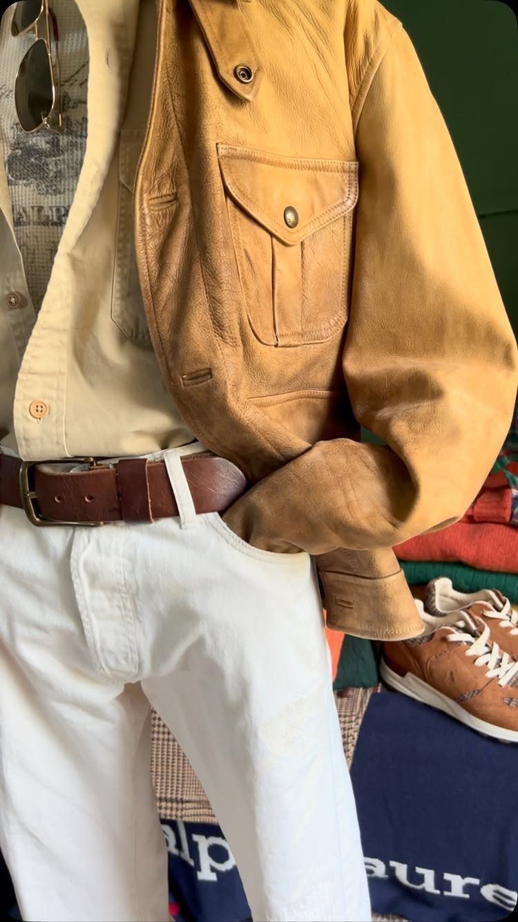 Tan leather jacket and beige shirt worn with white trousers and brown belt.