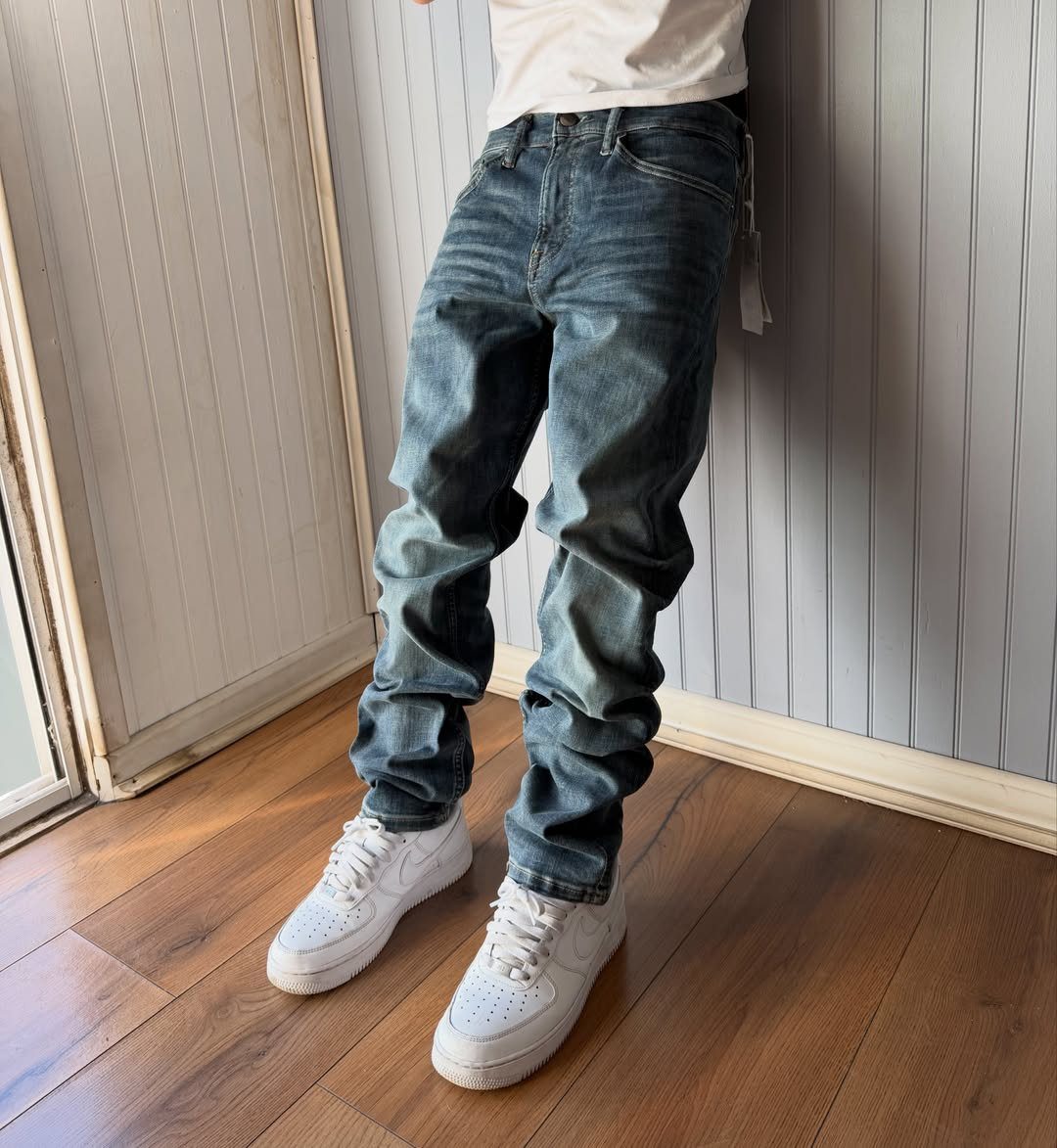 Person wearing loose blue denim jeans and white sneakers against a grey wall.
