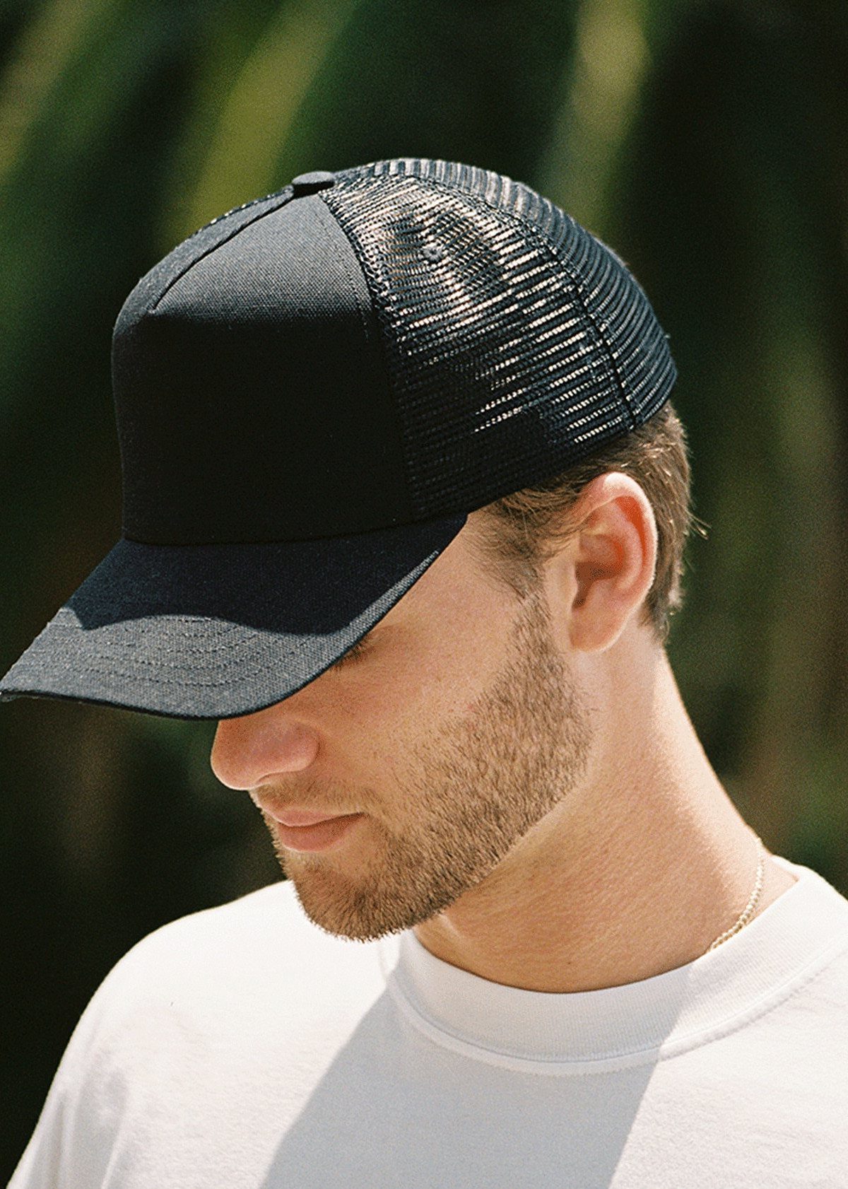 Man wearing a black trucker hat with mesh back and white t-shirt.