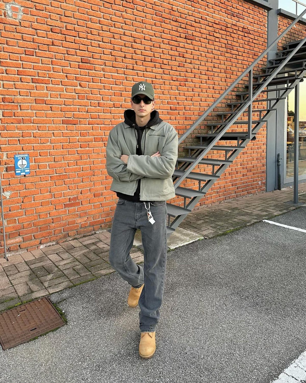 Man in grey jacket and jeans wearing tan work boots against brick wall