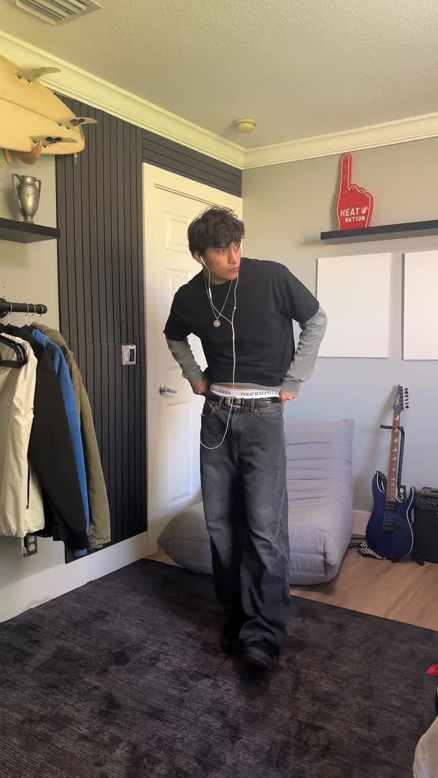 Young man wearing a layered t-shirt, baggy grey jeans, and a white belt.