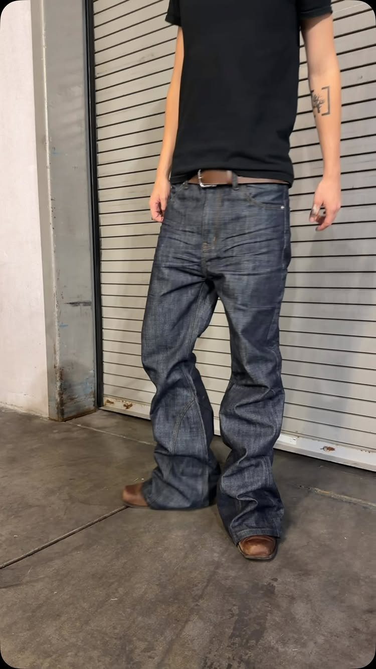 Man wearing dark blue low-rise flared skinny jeans and a black t-shirt.