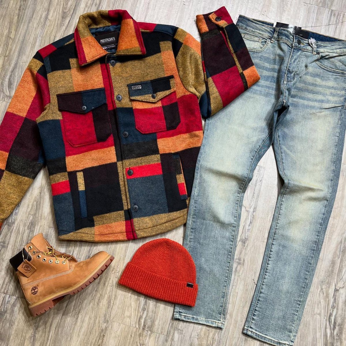 Multi-colored plaid jacket, red beanie, blue jeans, and tan boots on wooden floor.