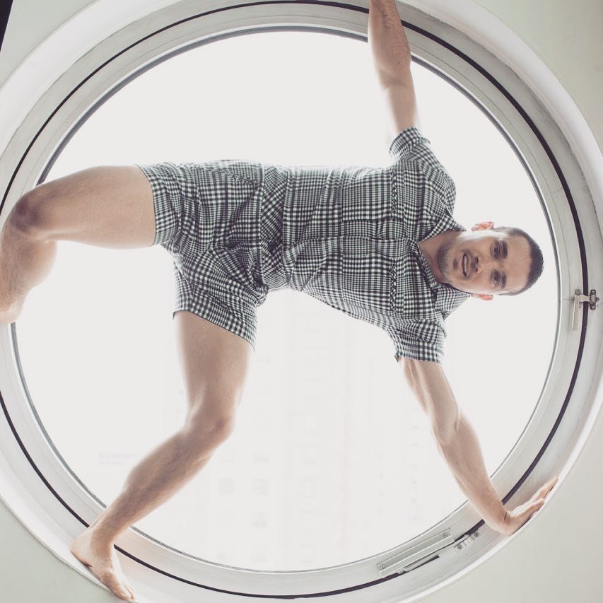 Man in checkered shirt and shorts posing inside a large circular window
