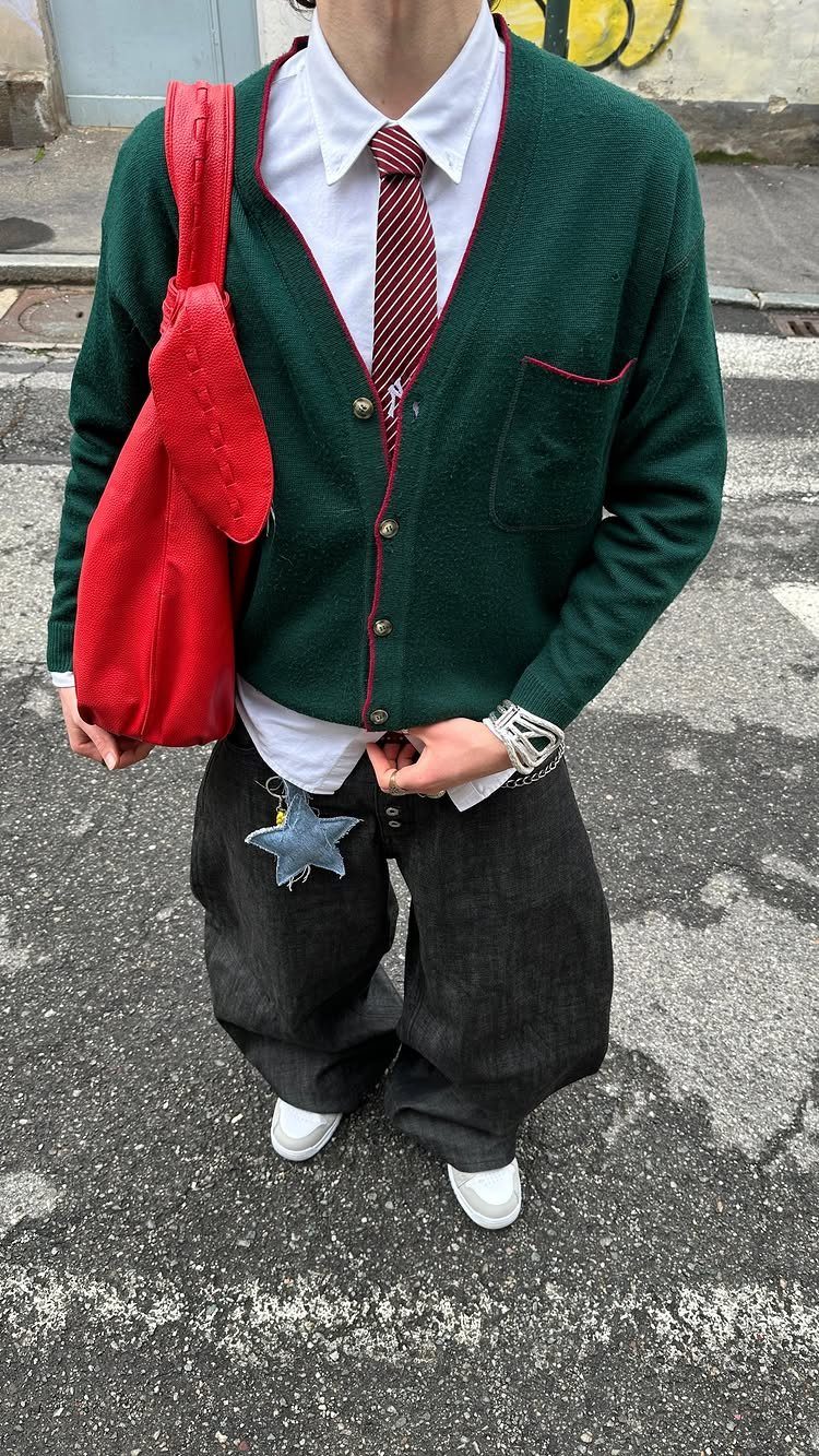 Person wearing a green cardigan and oversized baggy dark grey trousers on asphalt.