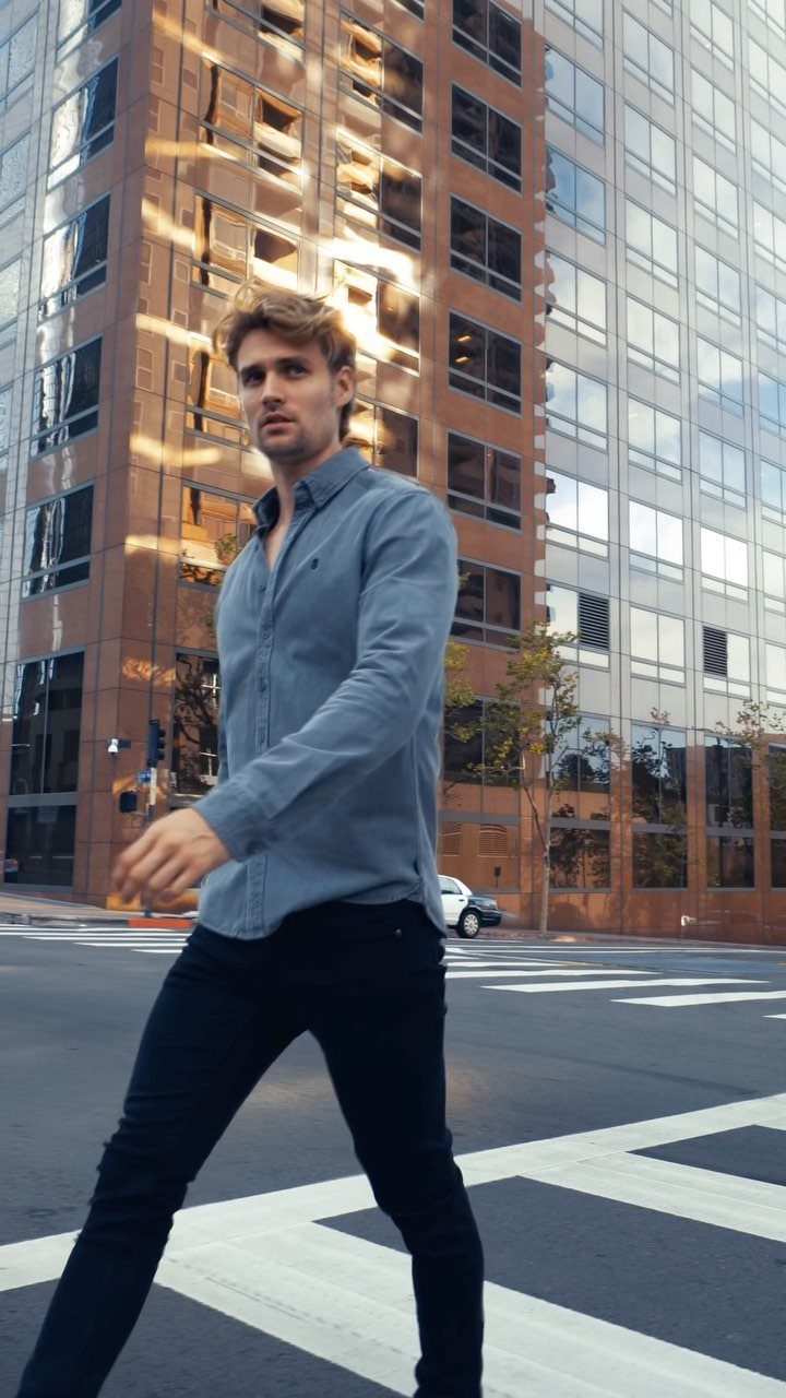 Man wearing a light blue denim shirt and black pants on a city street.