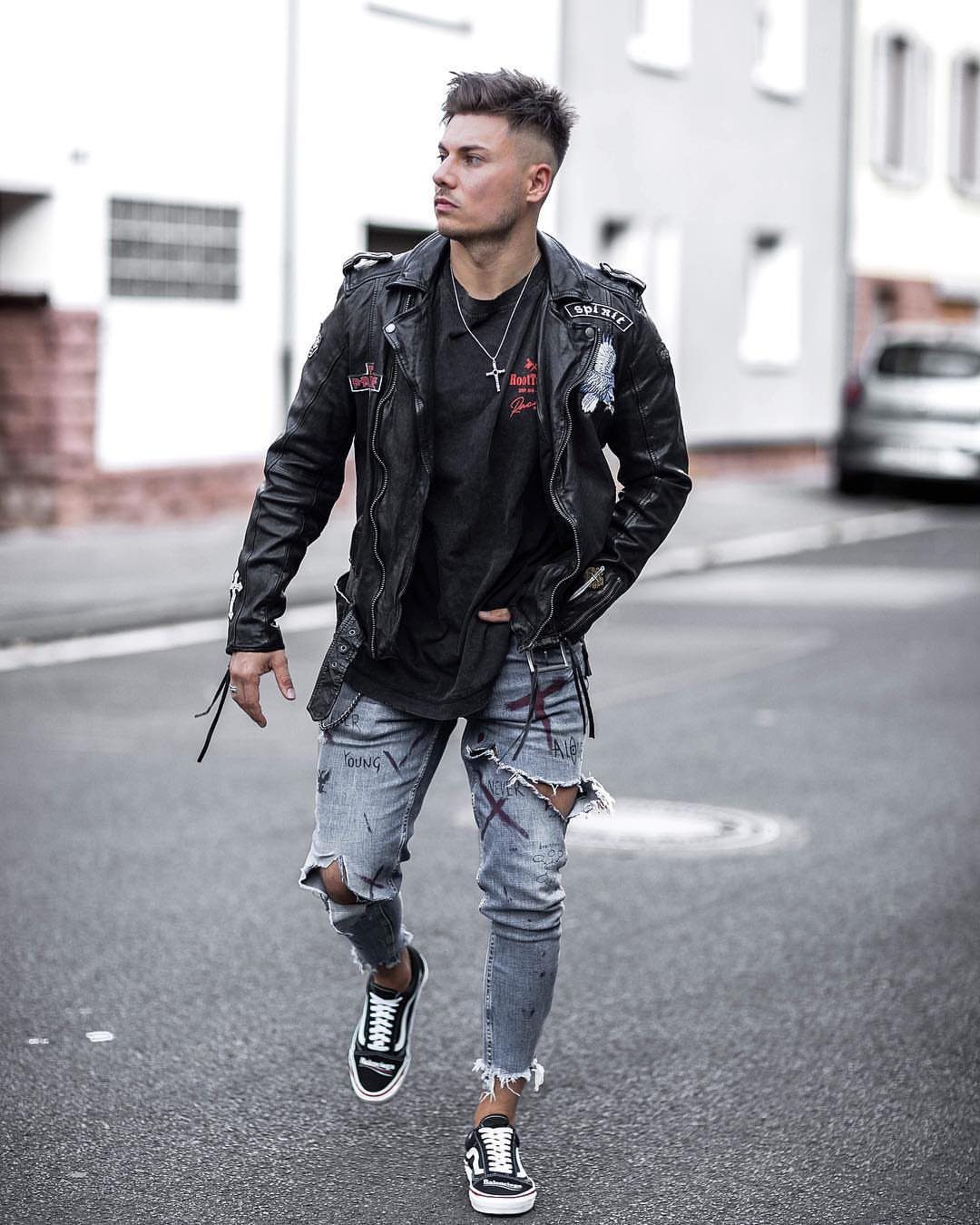 Man in black leather jacket and ripped light blue jeans standing on street