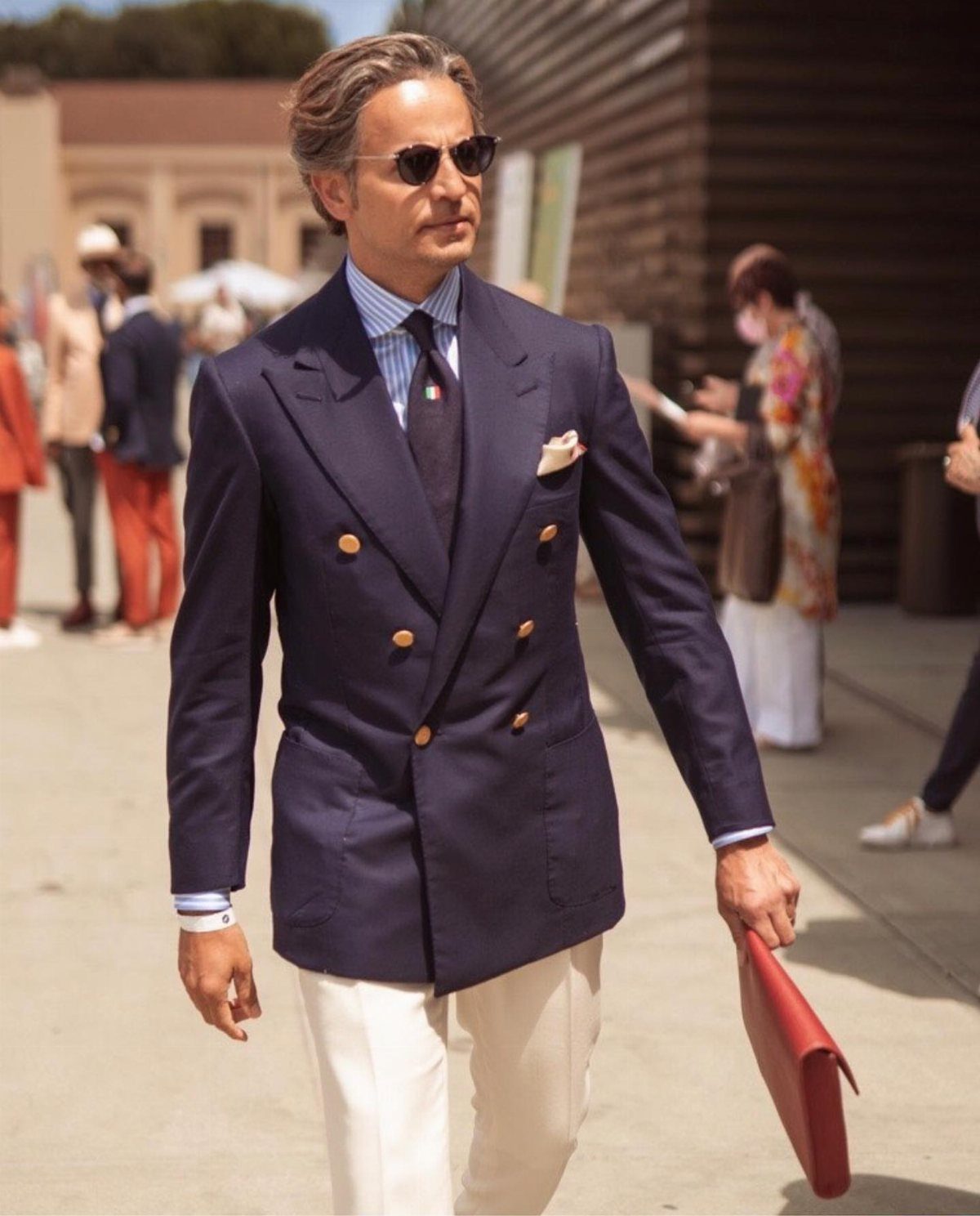 Man in a navy double-breasted blazer with gold buttons and white trousers outdoors.