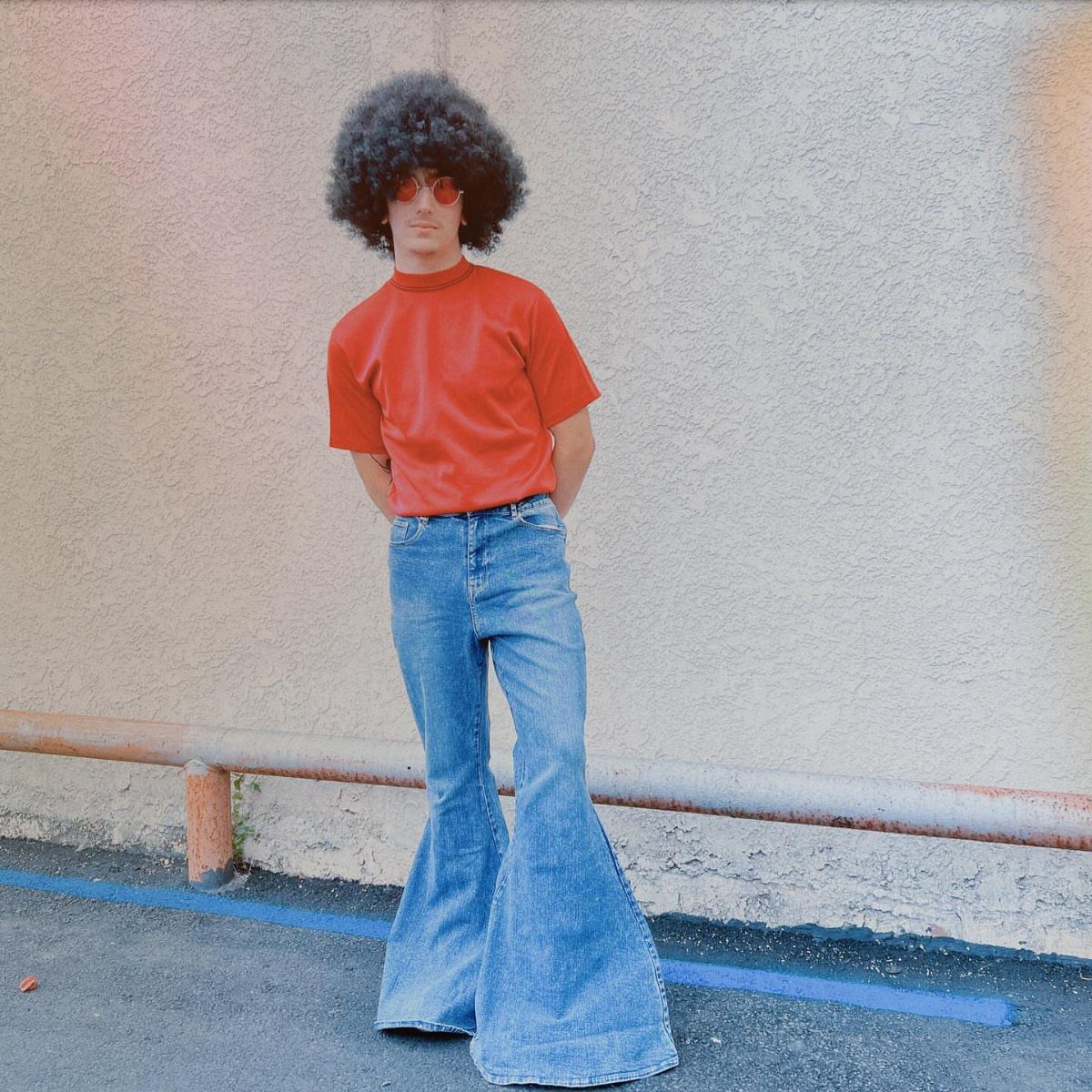Man with afro wearing red t-shirt and wide flared blue denim bell bottom pants.