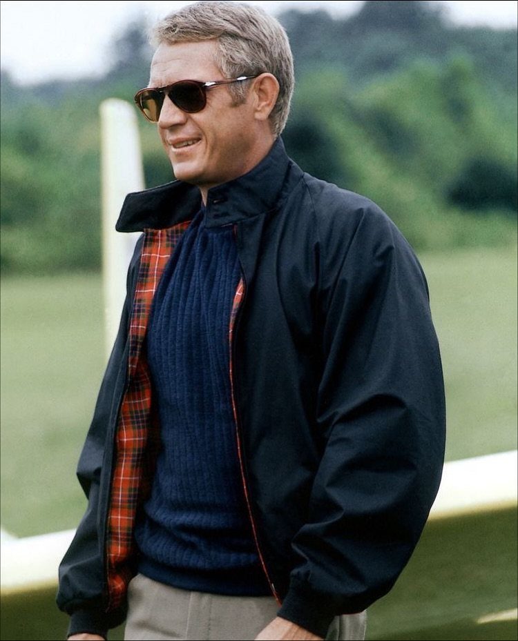 Man in 1960s style navy jacket with plaid lining and dark sunglasses outdoors.