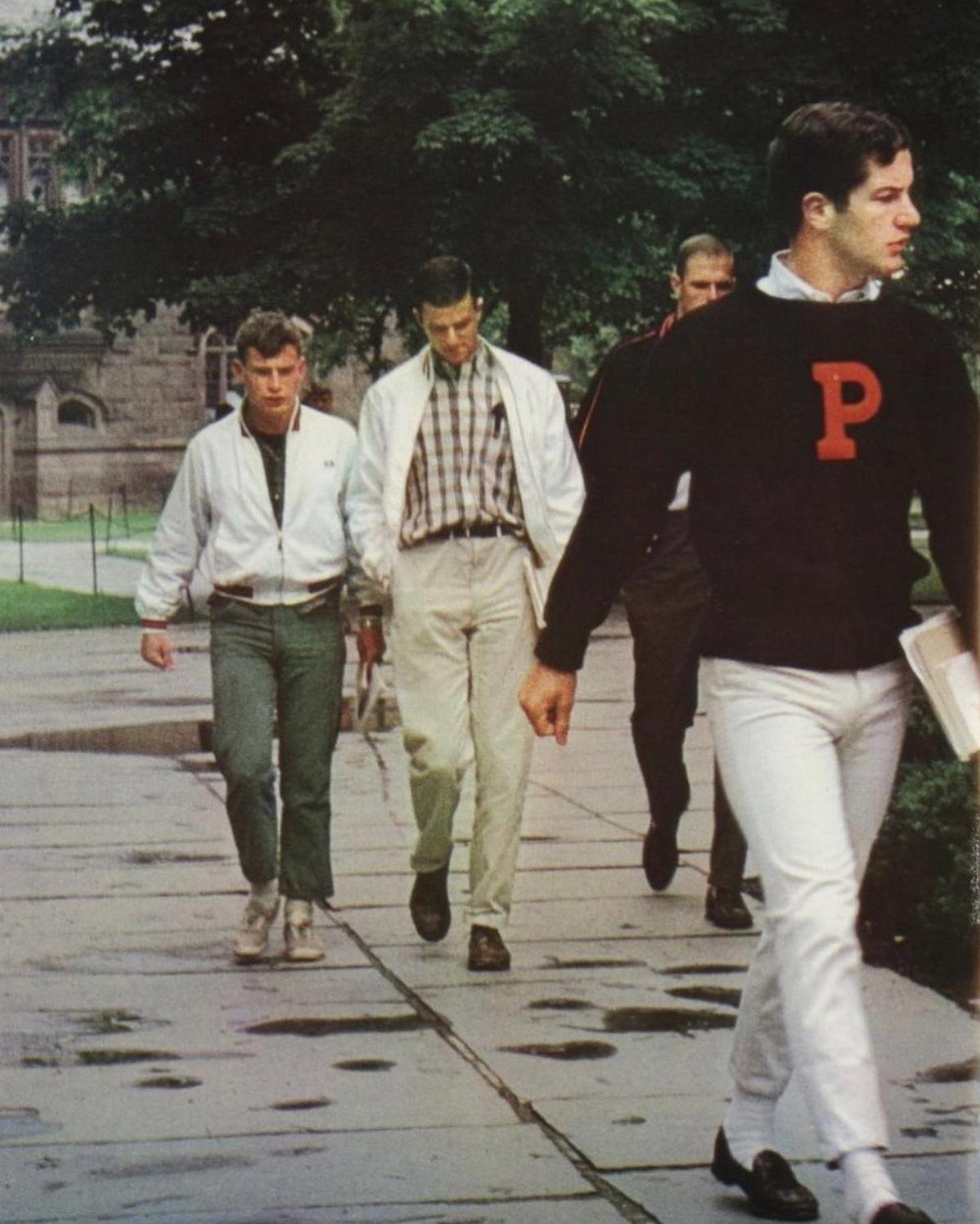 Four men walking outdoors wearing mid-century casual clothing and trousers on a sidewalk.