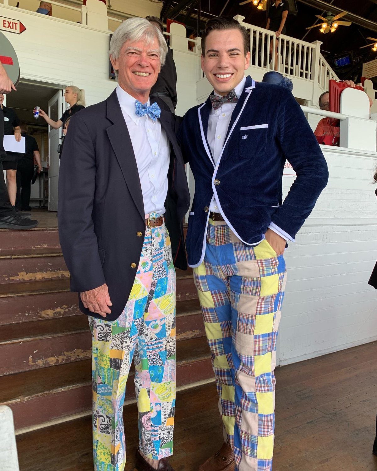 Two men wearing vintage style blazers and brightly patterned trousers standing on wooden stairs.