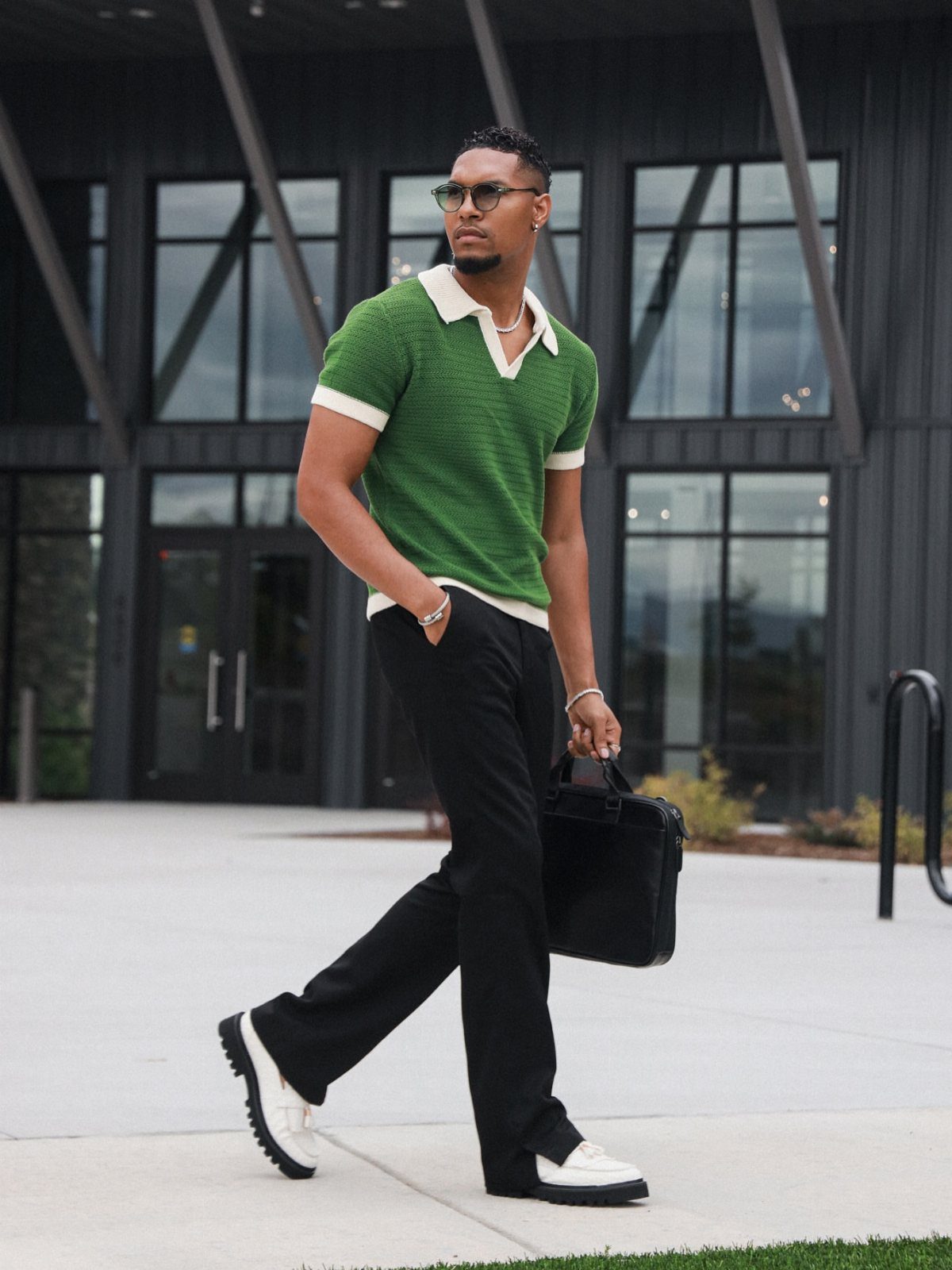 Man in green knit polo and black trousers walking with a briefcase