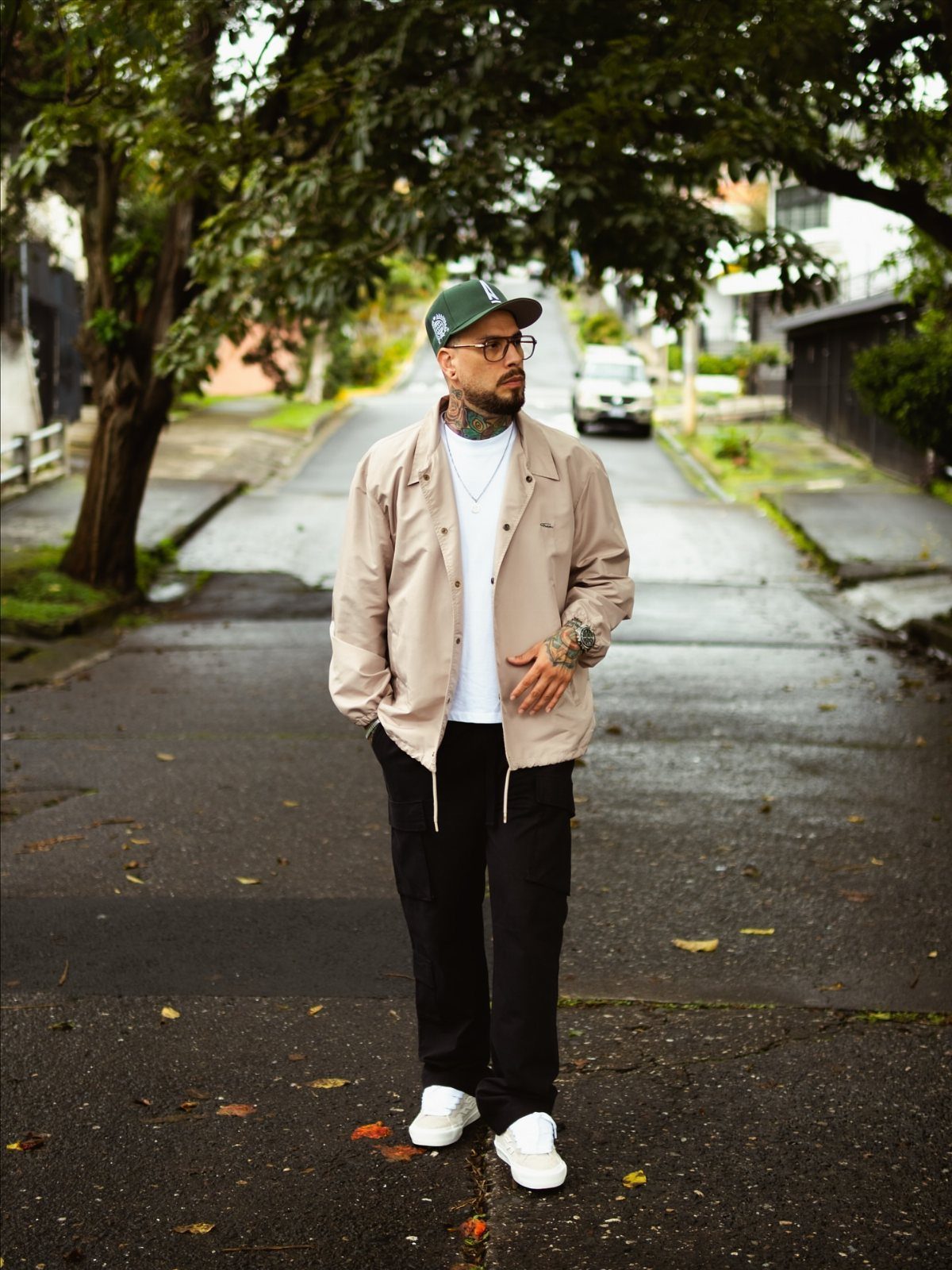 Man in beige jacket, black cargo pants, and green cap on a street.