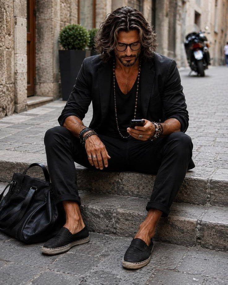 Man in all-black blazer and trousers sitting on stone steps in a city street