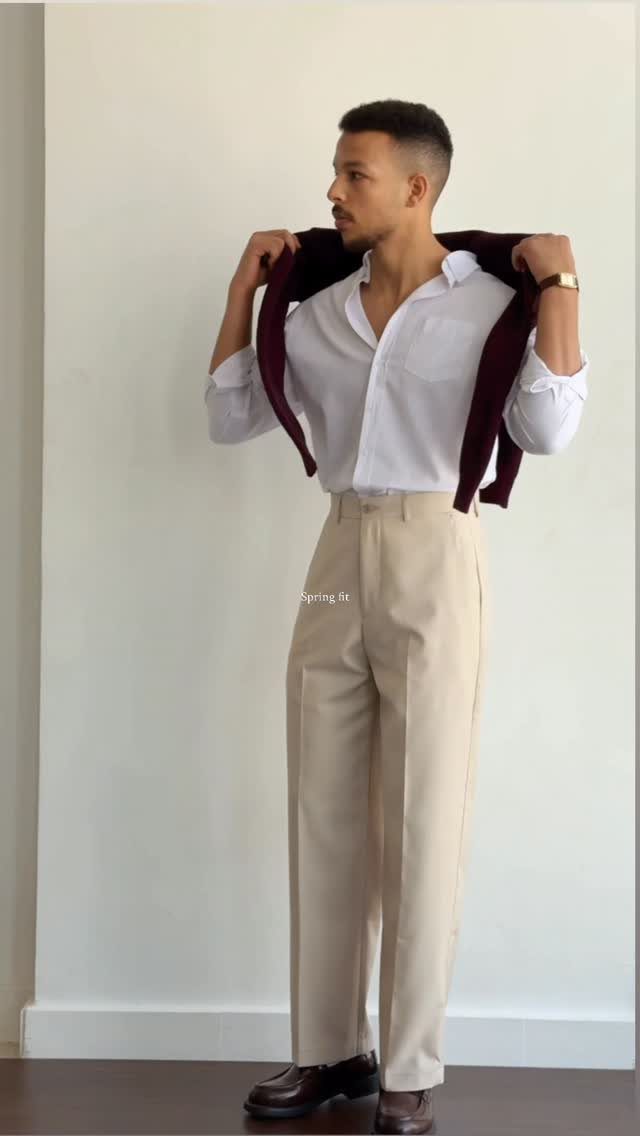 Man in white shirt and beige trousers with a burgundy sweater over shoulders.
