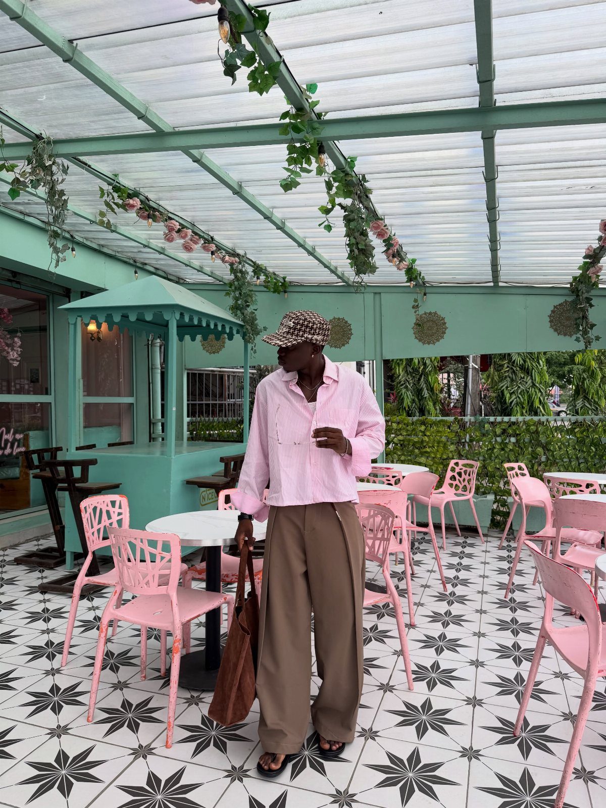 Man in pink striped shirt and tan trousers standing in a pastel cafe