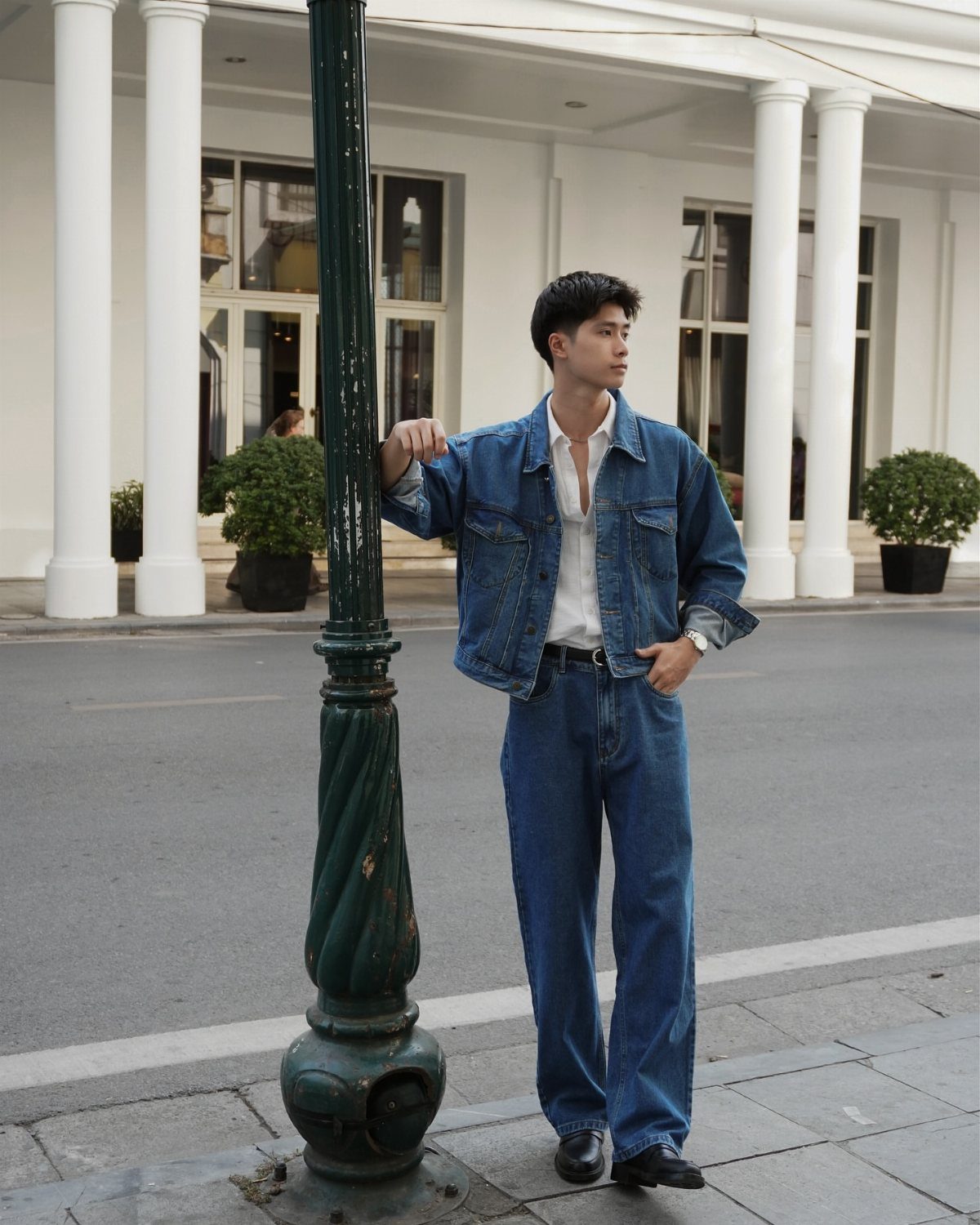 Man wearing a blue denim jacket, white shirt, and wide-leg denim jeans outdoors.